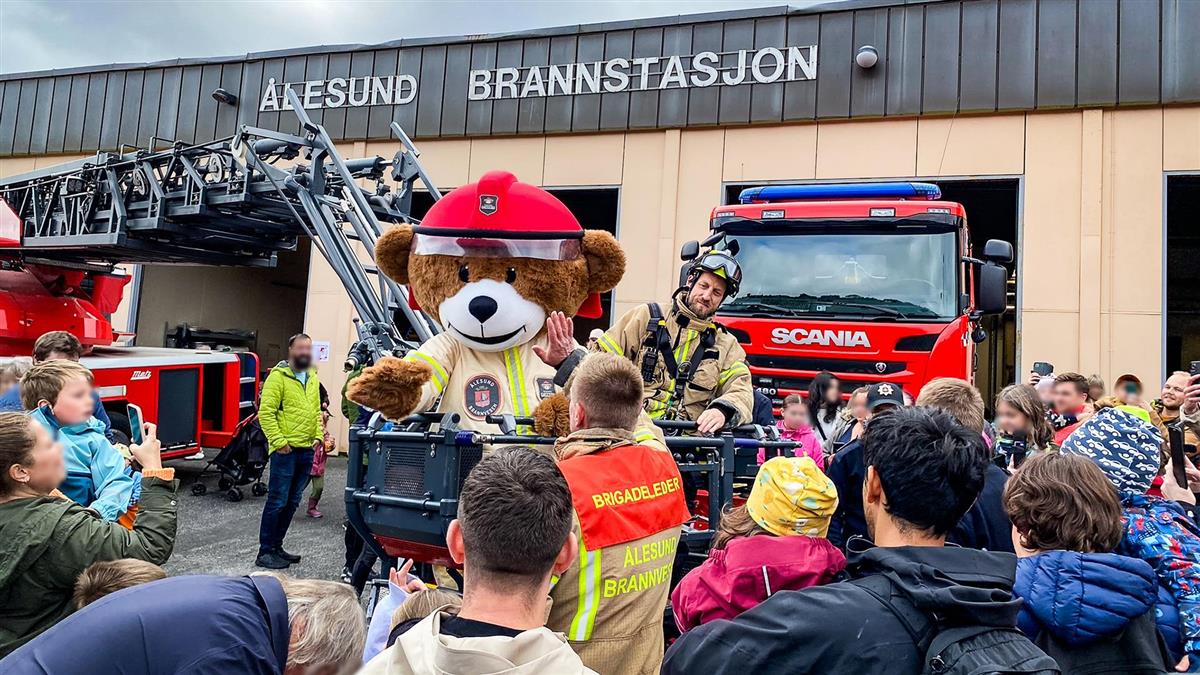 Åpen dag på brannstasjonen, brannbiler, brannbamse, brannkonstabler og publikum som hilser på - Klikk for stort bilde
